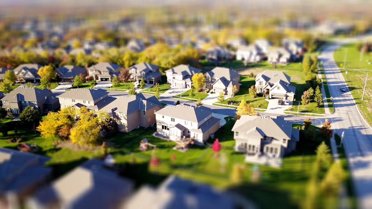 gallery-02 Tilt-shift aerial photo of a suburban neighborhood with green lawns and roads.